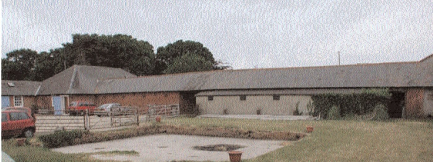 Long single-storey brick and slate farm buildings around a grassed courtyard, photographed in 2001
