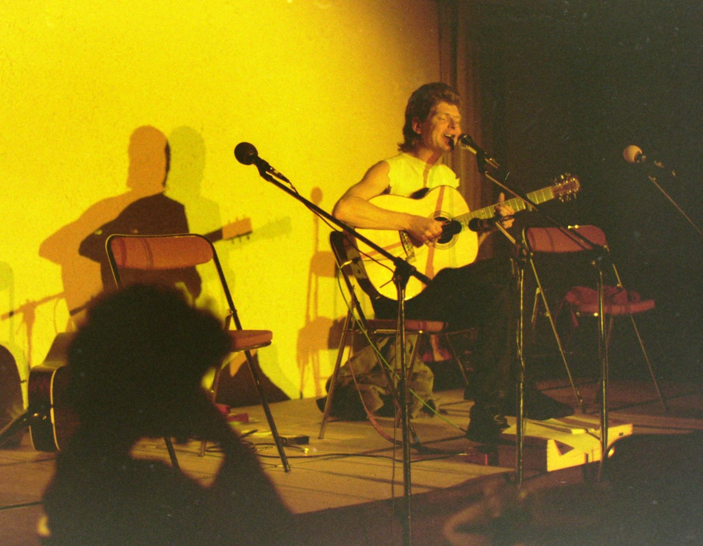 Young Dave Walters singing and playing an acoustic guitar on a stage lit in yellow
