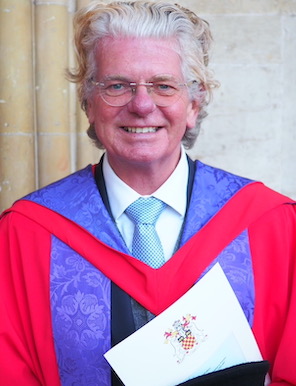 David Morgan Walters smiling, wearing red and violet doctoral robes outside a stone building