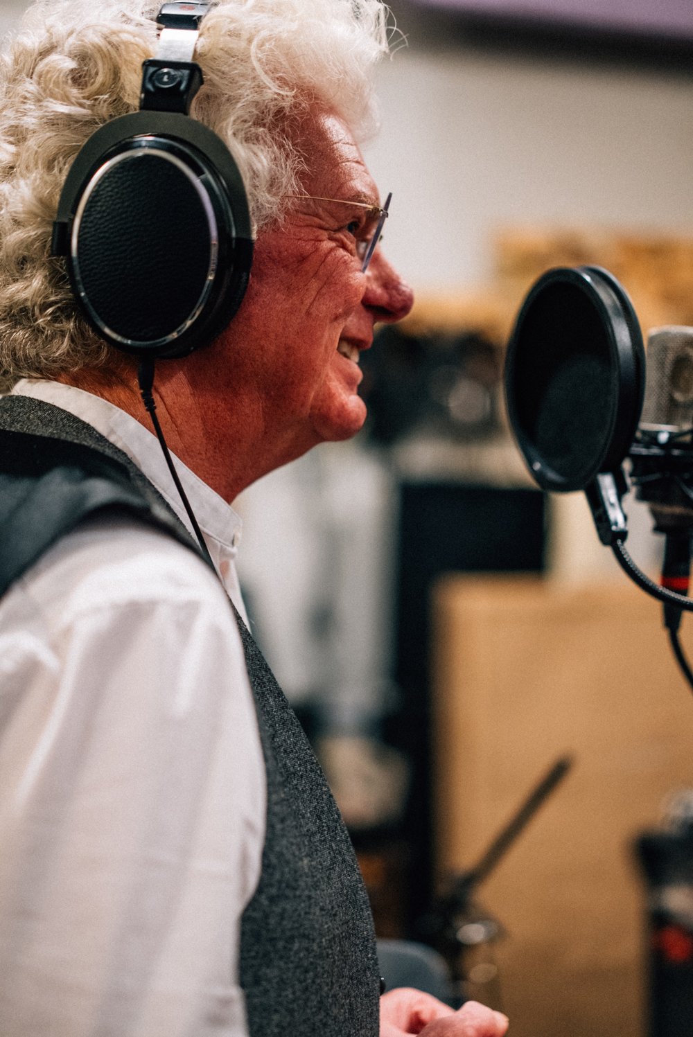 David Morgan Walters in profile, smiling, wearing headphones and singing into a studio microphone with a pop shield